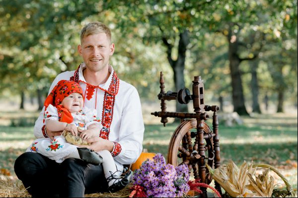 A father with his daughter posing on a stack of hey, having in the background a spindel