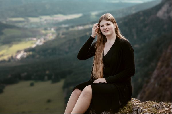 Mit dem weiten Tal im Hintergrund hält eine junge Frau ihr Haar und nimmt sich einen Moment Zeit, um die Energie des Berges zu spüren.