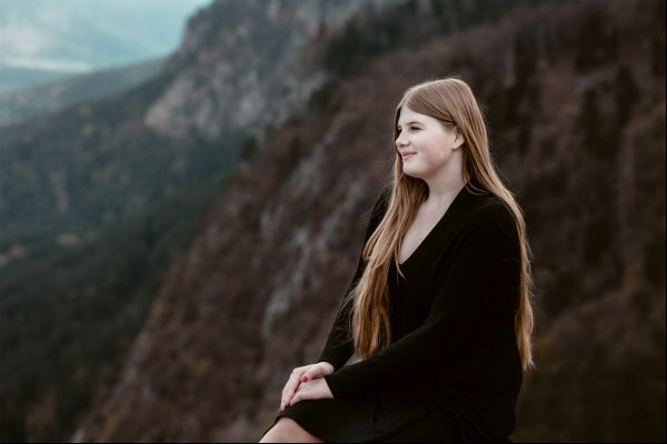 Mit Blick auf den Naturpark Hohe Wand sitzt eine junge Frau auf einem Felsen und nimmt sich einen Moment Zeit, um zu spüren, wie die Bergluft ihren Geist klärt.